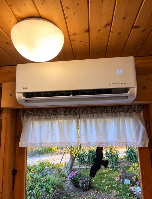 Nástěnná klimatizace Midea pod dřevěným stropem nad oknem chaty